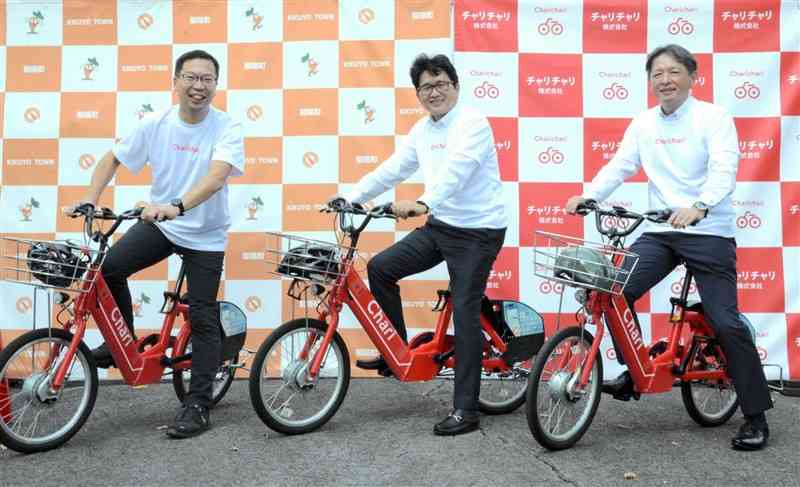 自転車にまたがるチャリチャリの家本賢太郎代表（左）と吉本孝寿町長（中央）、肥後銀行の前出洋取締役＝1日、菊陽町