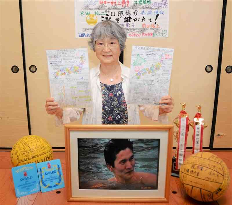 全国のプールを巡った日本地図を持つ日隈栄子さん。中央下の写真は次男の徳彦さん＝9月17日、熊本市中央区