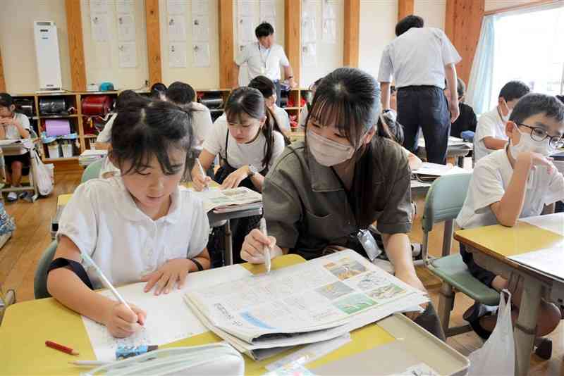 県立大の学生と一緒に新聞を読み、感想を書く三加和小の児童たち＝9月25日、和水町