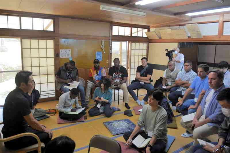 水俣市立水俣病資料館語り部の杉本肇さん（左）の話を聞く海外の行政官ら＝13日、水俣市