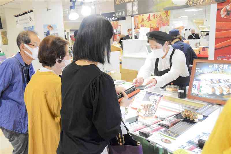 黄金色に焼き上げたサバと福井産コシヒカリを使ったすしを購入する買い物客＝16日、熊本市中央区