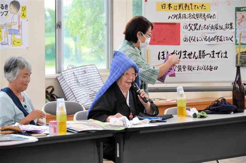 防空頭巾をかぶって空襲の様子を語る新日本婦人の会宇城支部の元松芳子さん（中央）。左は山田聰子さん＝3日、宇城市