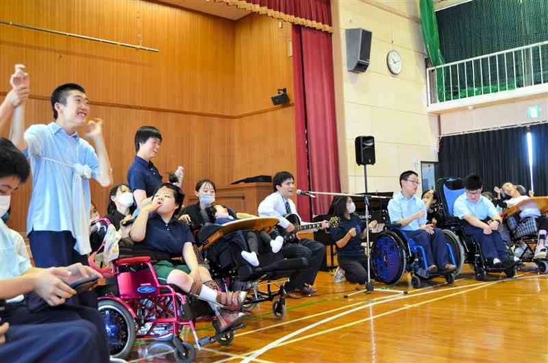 シンガー・ソングライター大山桂司さん（中央）のギターに合わせて防災ソングを歌う松橋支援学校高等部の生徒たち＝18日、宇城市