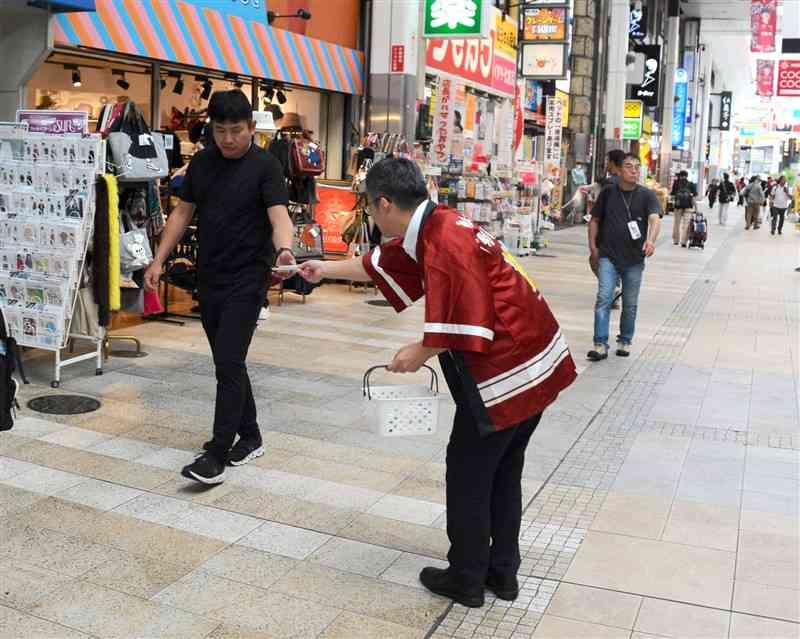 啓発用のウエットティッシュを配る熊本県選管の担当者（中央）＝19日、熊本市中央区