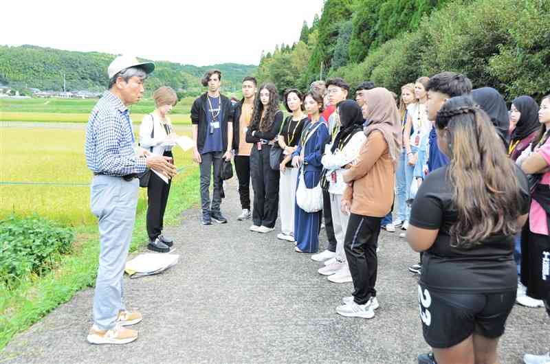 熊本地震で横ずれした断層が表出する堂園地区で、地元語り部の説明を聞く海外の高校生ら＝21日、益城町