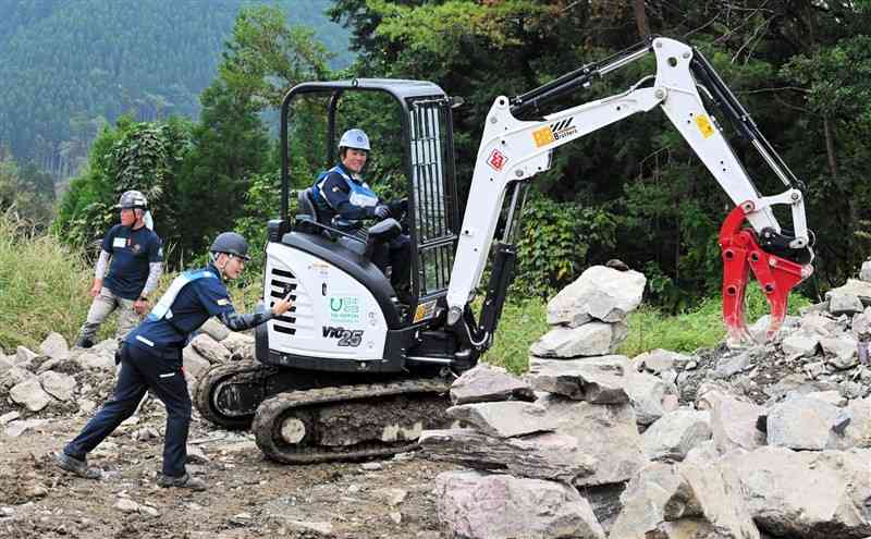 土砂災害を想定した訓練で、油圧ショベルを操作して岩を持ち上げる参加者＝24日、湯前町