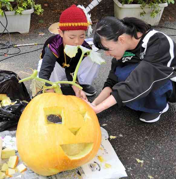 天草拓心高の生徒が育てた巨大なカボチャを使い、生徒と一緒にランタンを作る子ども＝26日、天草市