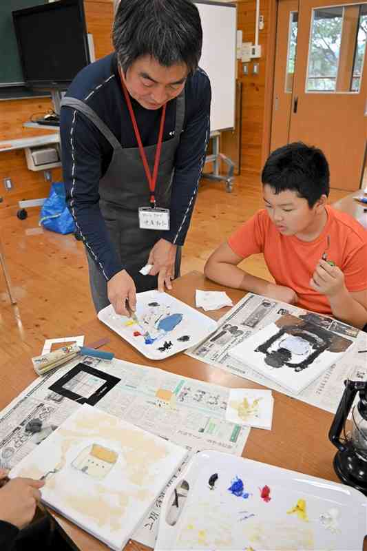 児童に色の塗り方を教える中尾和弘さん（左）＝10月28日、南阿蘇村