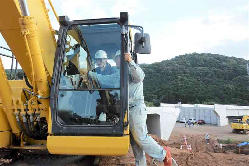 建設会社担当者（右）の指導を受けながら、油圧ショベルを操作する水俣高の生徒＝5日、水俣市