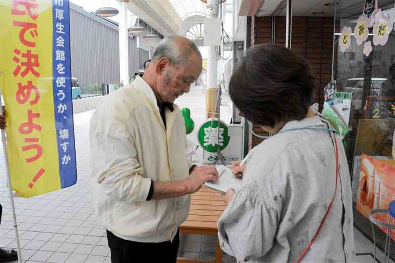 旧厚生会館の解体方針について賛否を問う住民投票実現に向けて進められる署名活動＝9日、八代市