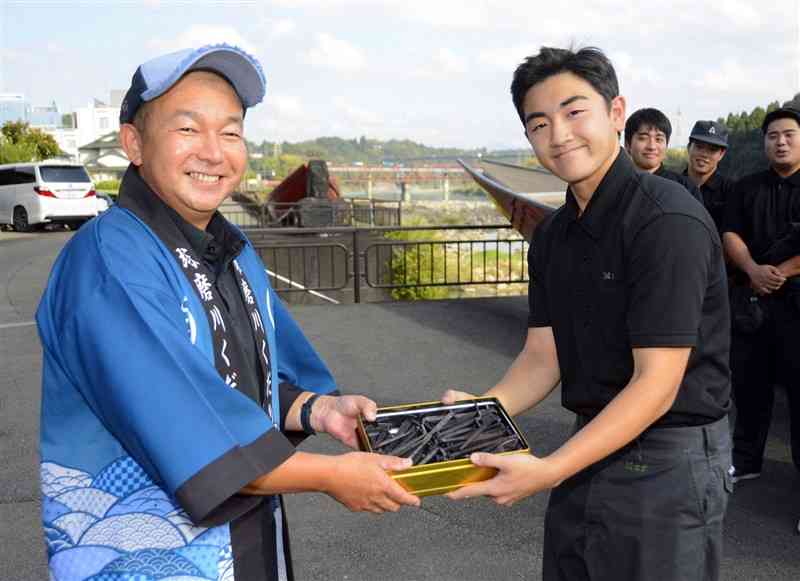 「球磨川くだり」の藤山和彦さん（左）に舟くぎを手渡す球磨工高3年の本武怜穏さん＝14日、人吉市