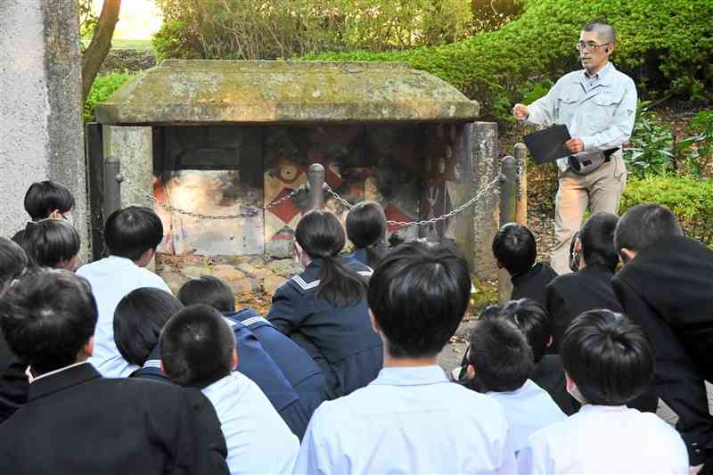 チブサン古墳を見学する前に、複製された石屋形の前で市職員から説明を受ける生徒たち＝19日、山鹿市