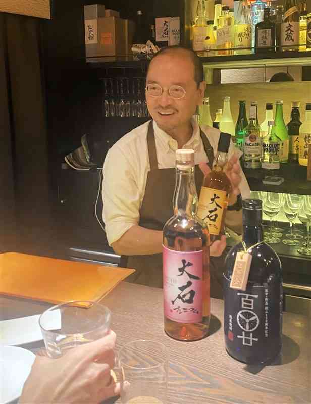 熊本県出身の客にお気に入りの球磨焼酎を薦める福島靖正さん＝東京都世田谷区