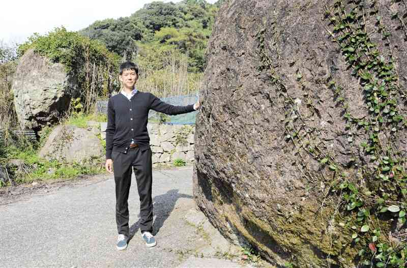 2度の地震を経て再会したといわれる「奇跡の夫婦岩」の間に立つ長谷川雅也さん＝熊本市西区