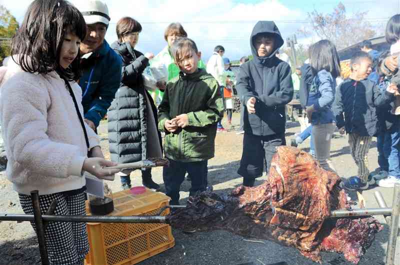 イノシシのかたまり肉にタレを塗るくまTOMOサポーター（左）