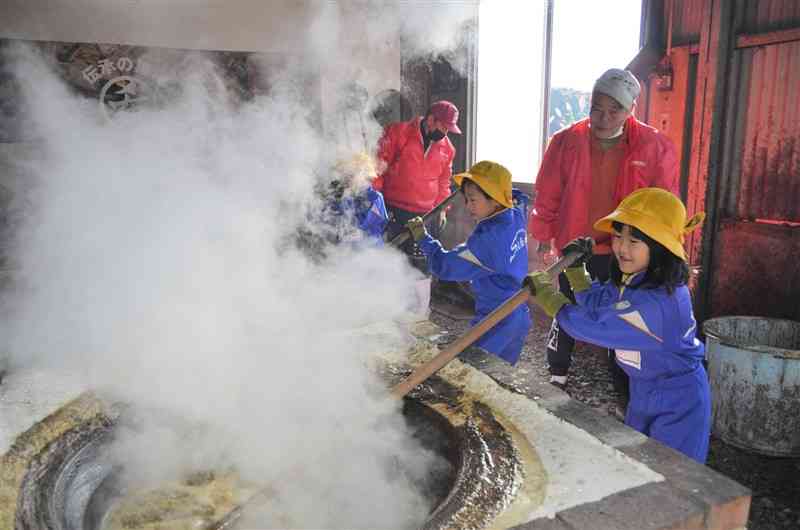 サトウキビの搾り汁を大釜で煮詰める青海小の児童たち＝1日、宇城市