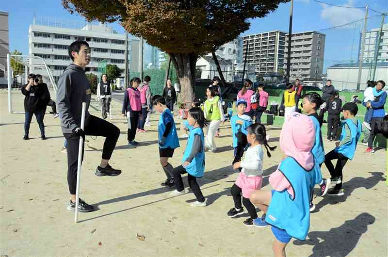 くまTOMOサポーター親子に速く走るコツなどを伝える熊本学園大の髙橋恭平准教授（左）＝11月30日、熊本市中央区