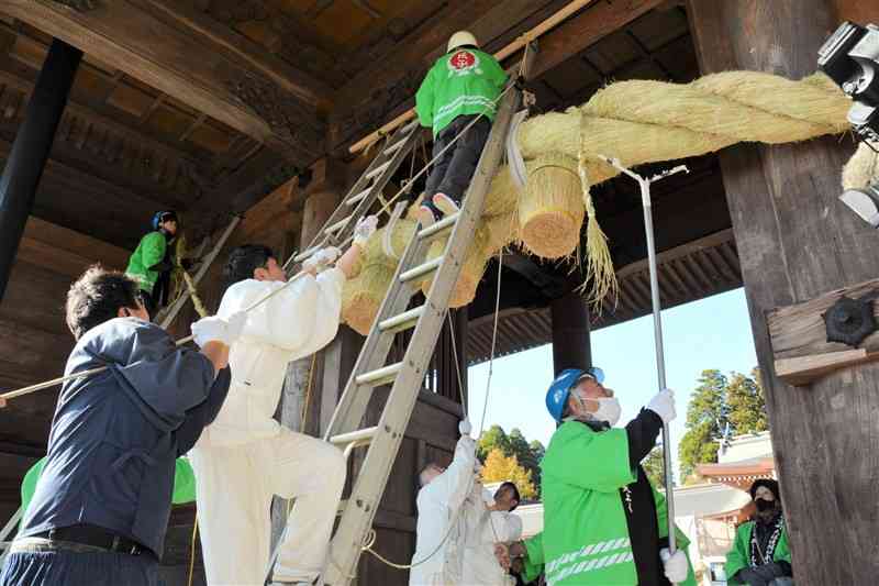 阿蘇神社の楼門に大しめ縄を飾り付ける「一の宮町大注連縄伝承会」の会員ら＝9日、阿蘇市