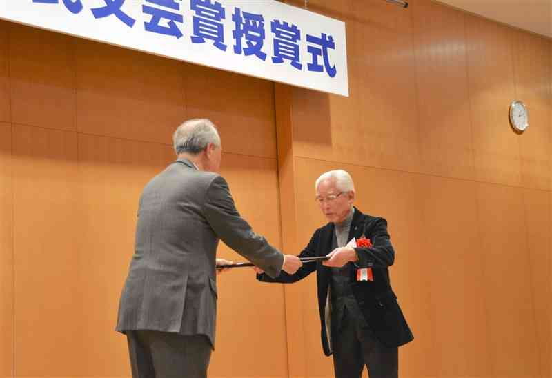 賞状を受け取る評論・ノンフィクション1席の中川誠之さん（右）＝12日、熊本市中央区