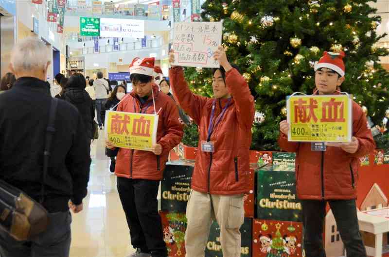 サンタクロースの格好で買い物客に献血を呼びかける大学生＝15日、嘉島町