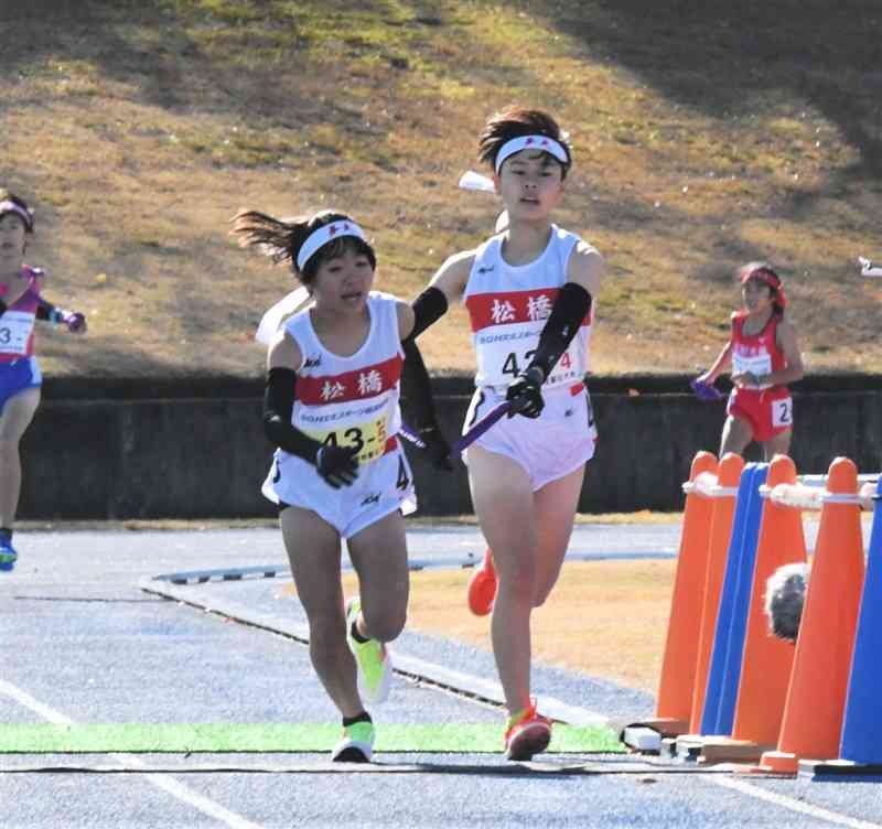 女子松橋の4区・緒方柚月（右）からたすきを受けスタートを切る5区の坂田遥香＝滋賀県の希望が丘文化公園