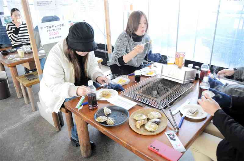 鏡オイスターハウスでカキの炭火焼きを楽しむ来店客＝20日、八代市