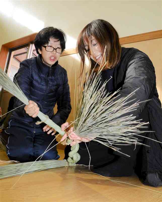 イ草の束を編んで縄を作る親子＝20日、熊本市中央区