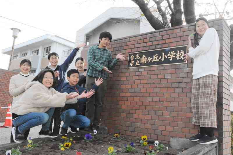 校門のプレートを囲む南ケ丘小の児童と教職員＝12月20日、合志市