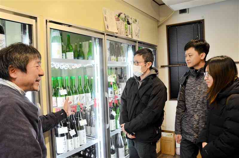 来店した台湾の客に日本酒の説明をする「たわらや酒店」の宇野功一さん（左）＝2024年12月21日、菊陽町