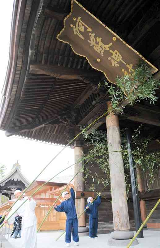 竹を使って楼門のすすを払う阿蘇神社の神職ら＝26日、阿蘇市