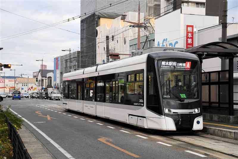 健軍町電停に停車する市電の新型車両。一帯では交差点の拡張や電停の改良が計画されている＝2024年12月、熊本市東区