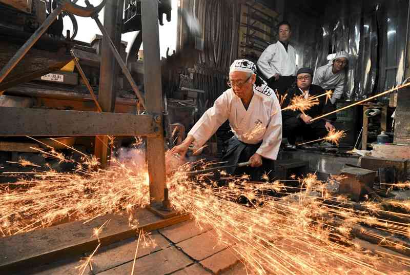 ハンマーで鋼を鍛える松永源六郎さん（左）＝3日、荒尾市