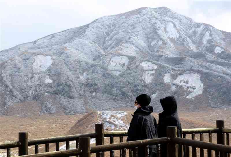 積雪した烏帽子岳を眺める観光客＝8日、阿蘇市