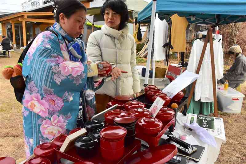 能登半島地震の被災地支援のために開かれたマルシェで、輪島塗の漆器を手に取る来場者（左）＝12日、熊本市東区