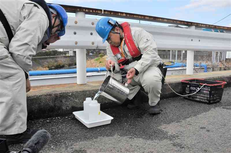 坪井川から採水して検査容器に移す業者＝15日、熊本市北区