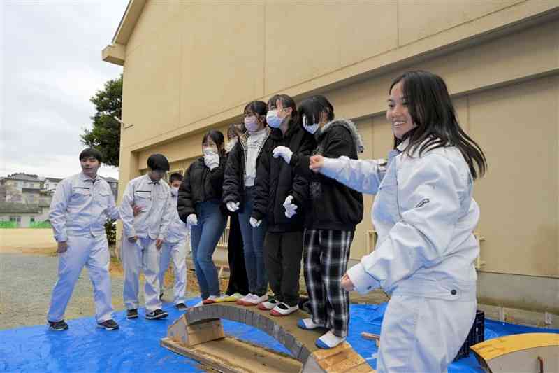 完成した眼鏡橋に、5人で乗って強度を確かめる児童たち＝16日、荒尾市