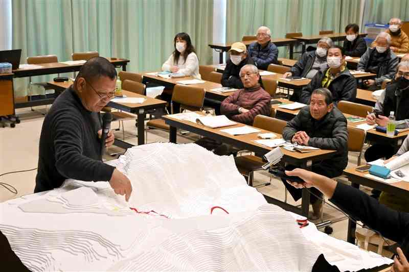 地形模型を使って、堀切門への登城道の想定ルートなどを説明する温故創生館の宮崎敬士課長（左）＝26日、山鹿市