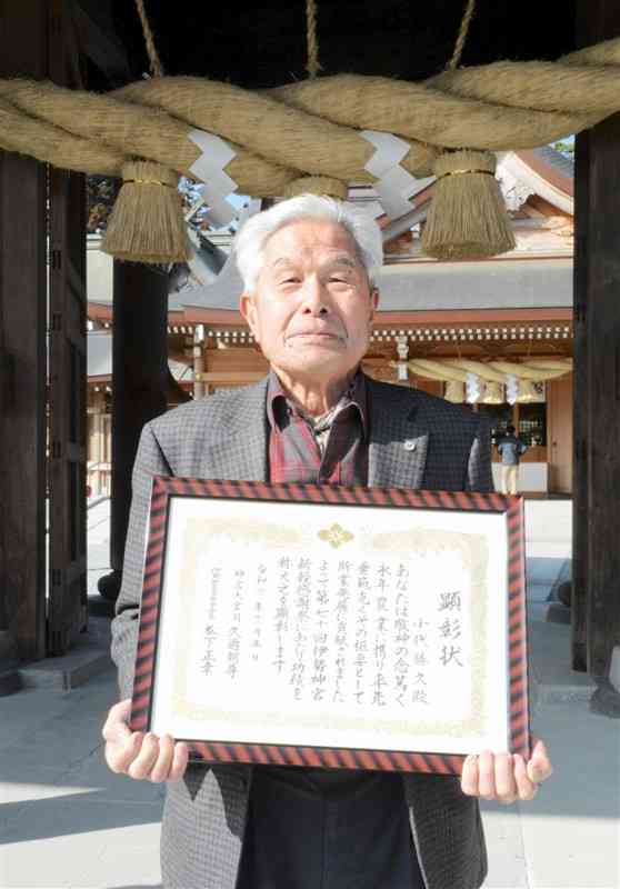 阿蘇神社でしめ縄の前に立つ小代勝久さん。伊勢神宮の関係団体から農事関係功労者として熊本県内で初めて顕彰された＝25日、阿蘇市