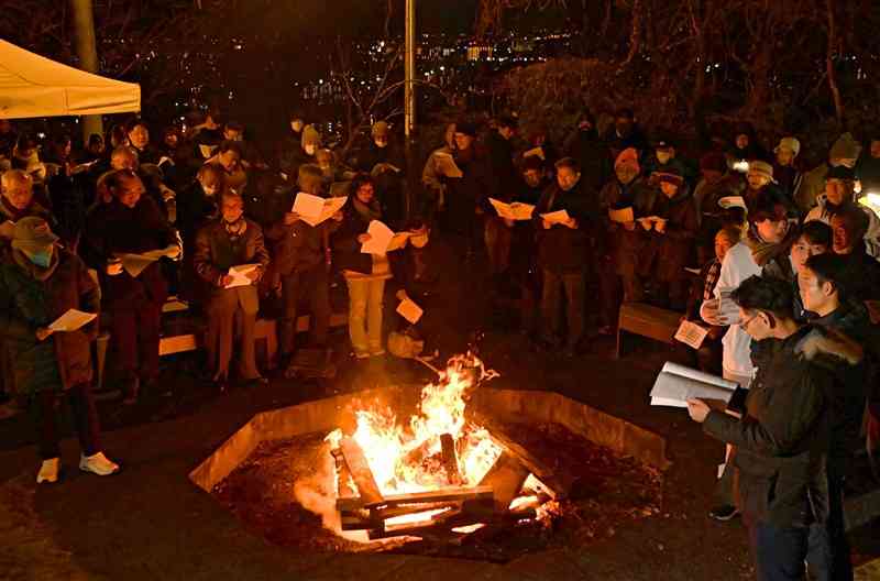 「熊本バンド」をしのぶ早天祈祷会で、たき火を囲み賛美歌を歌う参加者たち＝30日午前6時30分ごろ、熊本市西区の花岡山（小野宏明）