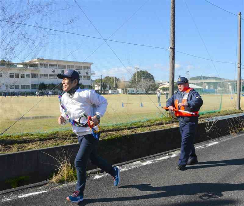 警察官（右）からバトンを受け取って走り出す地元郵便局長＝１月30日、芦北町