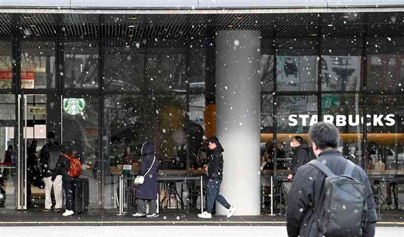 雪が舞うJR熊本駅前を行き交う人々＝4日午前8時40分ごろ、熊本市西区（石本智）