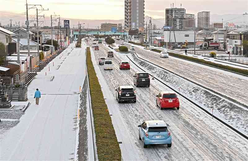 雪が積もった県道熊本港線で、スリップしないようにゆっくり走る車列＝8日午前7時10分ごろ、熊本市南区（石本智）