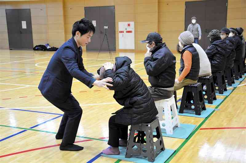 転倒防止のため座ったままできるトレーニングを高齢者に教える星子豊英さん（左）＝7日、熊本市北区