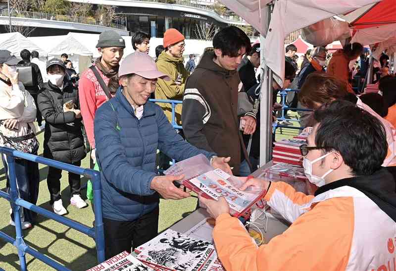 熊本城マラソンの出場受け付けが始まり、ナンバーカードなどを受け取るランナーたち＝14日正午過ぎ、熊本市中央区の花畑広場（上杉勇太）